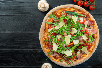 Homemade fresh Pizza with jamon, arugula, parmesan and cherry tomatoes on a black wooden with copy space. Top view food photo. Flat lay. Italian cuisine.
