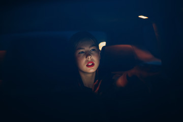 Young woman sitting in back seat of car vehicle at night. Taxi concept.