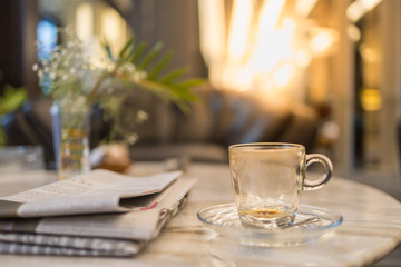 Close up of empty and drity glass cup of hot coffee with plate on table with newspaper in the living room.