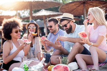 Happy friends eating watermelon on beach