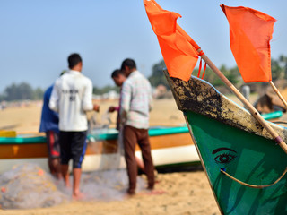 The fishermen are fixing nets to beside the traditional fishing boat on the beach, Gokarna, India.