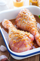 Raw turkey drumstick in mustard-honey marinade in enameled form on a wooden table, selective focus