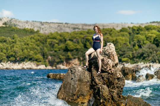 Girl in a swimsuit on the rocky beach, turquoise water of the Adriatic Sea. Sea sports, freedom, vacation