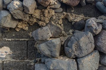 Lava brick wall decorated with cobblestones partially fallen off and hardened cement