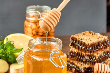 honey in honeycombs on a wooden plate and golden honey in a jar with nuts and comb for honey with lemon and ginger on a brown wooden background