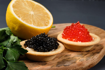 Naklejka na ściany i meble tartlets with red and black caviar on a wooden board with lemon and herbs on a gray background. Close-up