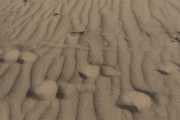 Fancy pattern on dry sand created by wind and human footprints close-up shot