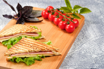 Half of a sandwich in the form of a triangle on a wooden board. The sandwich is decorated with a lettuce leaf and cherry tomatoes.