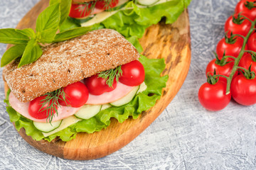 Sandwich with cheese, cucumber and Cherry Tomato on a wooden board. The sandwich is decorated with a lettuce leaf and cherry tomatoes.
