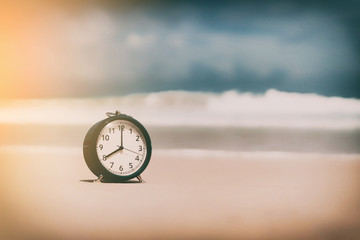 Clock on sand beach with smooth wave background.