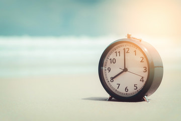 Clock on sand beach with smooth wave background.