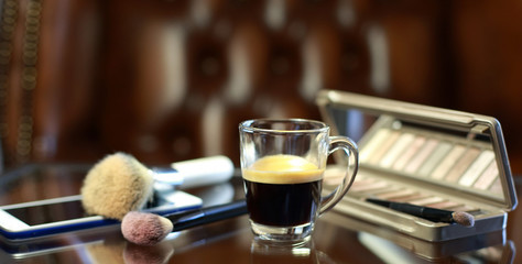 Cup of coffee with the phone and make-up set, shadow palette, and brushes