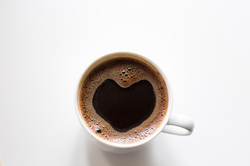 white mug with freshly brewed coffee, with a foam on the surface in the shape of a heart