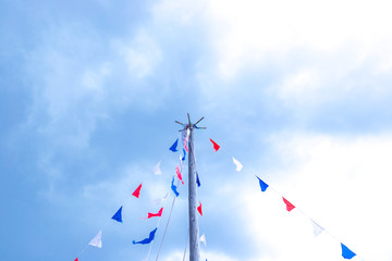 holiday flags hanging on a mast against a blue sky with clouds