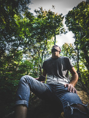 Obraz premium Young guy resting on a trunk in the forest and enjoying the pure air