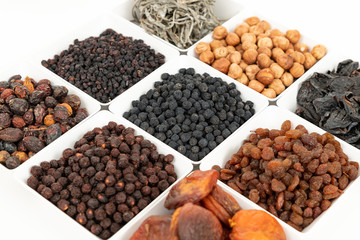 Groups of various kinds of dried fruits in square white bowls on white background