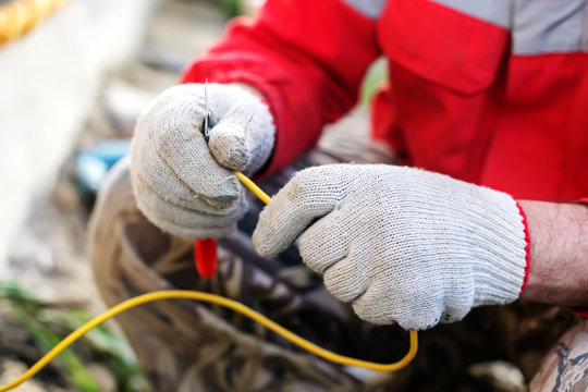 Master Electrician Connecting Ground Wire To The Metal Rod Near Dwelling House. Electrical Worker Hands Fixing Cable To Earth Bonding Bar. Man Builder Constructing Earth Grounding System.