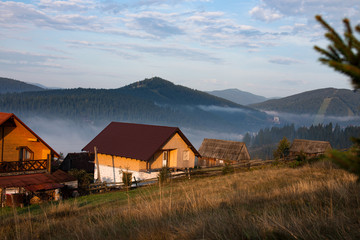 Fototapeta na wymiar Early foggy morning in the mountains. Carpathians, Bukovel, lawn houses.