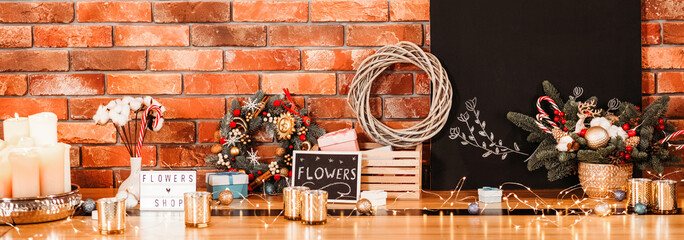 Flowers shop. Festive gift decoration. Mockup black chalkboard. Candles and fairy lights on wooden surface. Brick wall background.