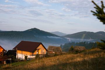 Fototapeta na wymiar Early foggy morning in the mountains. Carpathians, Bukovel, lawn houses.
