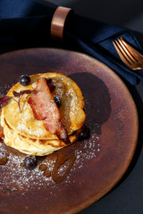 american pancakes with bacon and blueberries with bronze knife and fork and blue napkin