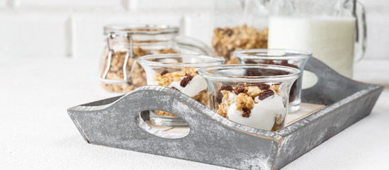 Grnola, raisins, milk in glass jars and various ingredients for a super meal with copy space on a light background
