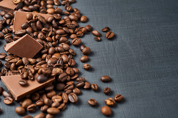 Heap of broken pieces of bitter or milk chocolate and fried coffee beans scattered on dark scratched concrete table. Space for text