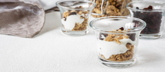 Grnola, raisins, milk in glass jars and various ingredients for a super meal with copy space on a light background