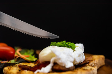 Homemade meal, Organic egg benedict with fresh salad and knife ready to eat on wood plate for healthy breakfast in dark background