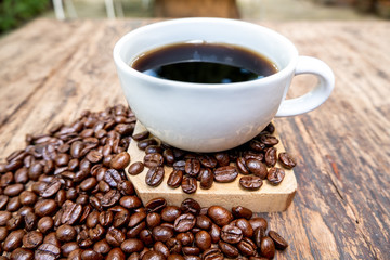 full of coffee beans spilling out bag on brown wooden background with a cup of black coffee