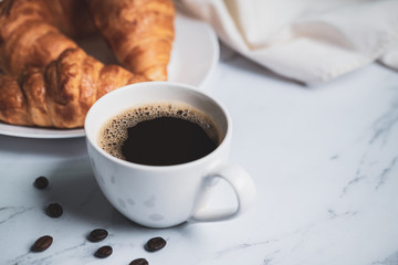 Breakfast with fresh croissants and cup of black coffee on wooden board