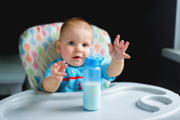 Funny  boy of 10 months drinking milk from a bottle in the kitchen at home. Baby food, dairy food concept.	