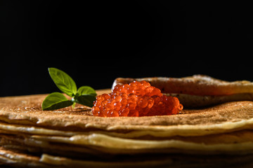 Stack of pancakes with red caviar on black background, close up