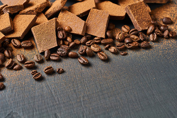 Heap of broken pieces of bitter or milk chocolate powdered of cocoa and fried coffee beans scattered on dark scratched concrete table. Space for text