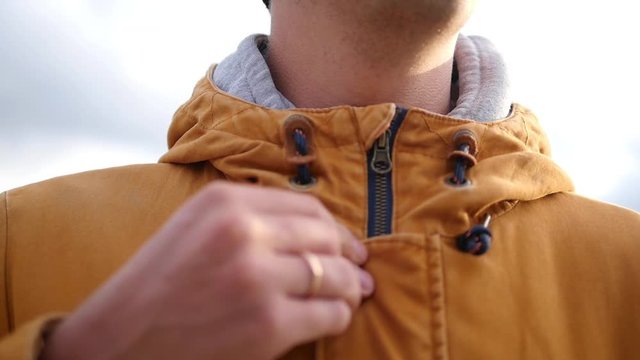 Man fastens a zipper on a jacket in cold autumn day. Sunset