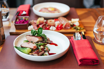 Roasted Duck Breast with Bok Choy served with duck sauce with cold cuts in background.