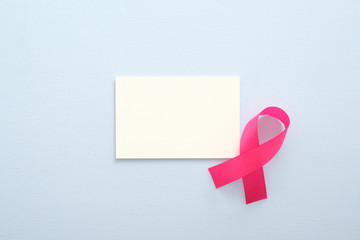 Breast cancer awareness month concept. Empty paper card mockup and pink breast cancer ribbon on blue background.