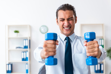 Young handsome employee doing sport exercises at workplace