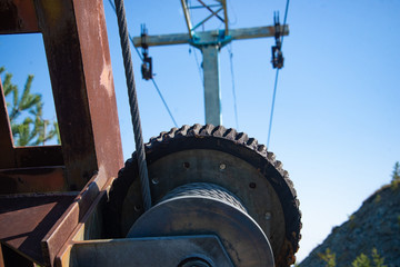 Steel cable and winch. Part of an old winch with a steel rope on a lift. Detail of the cableway. Close-up view of steel big wheel of cableway in mountains against the blue sky.