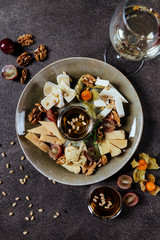 Cheese plate: Parmesan, cheddar, gouda, mozzarella and other with basil on wooden board on dark background. Tasty appetizers. Top view.