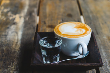 close up modern hot black coffee the cappuccino on wood background with coffee bubble foam pattern and texture in white cup looking and feel so delicious on glasses table in coffee shop.