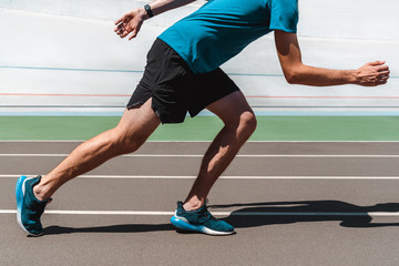 partial view of athletic young sportsman jogging on running track