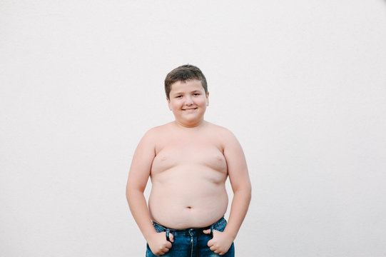 overweight concept of happy smiling fat little caucasian kid in jeans standing on bright wall background with copy space