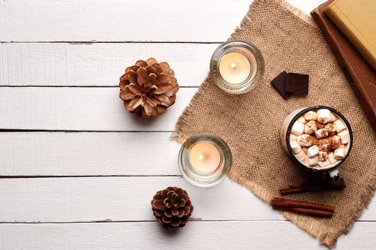 Cup of hot cocoa or hot chocolate with marshmallows and cinnamon sticks on wooden background with burning candles. Rustic. Winter mood. Flay lay.