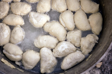 Dumplings are boiling in cauldron. Preparation of Ukrainian traditional dish on fire.