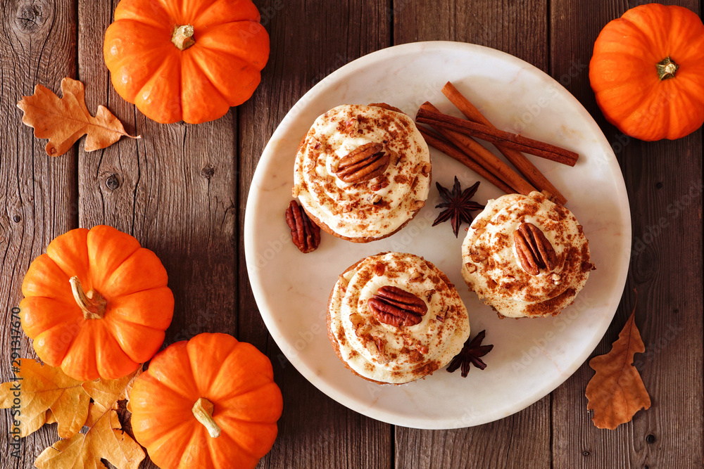 Poster autumn pumpkin spice pecan cupcakes with creamy frosting. top view table scene over a dark rustic wo