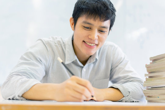 close up high school student man hand writing by mark  choices on answer sheet paper for final examination test in classroom concept