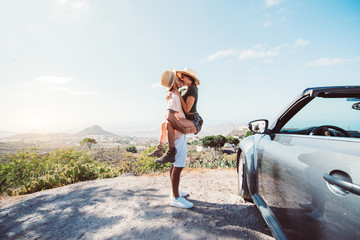 Couple in love kissing on a cliff at road trip with a convertible car