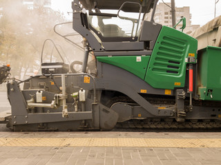 Tracked paver. Industrial pavement truck laying fresh asphalt on construction site. Asphalt a new on the road texture and a tractor on laying of asphalt. Road works flooring asphalt laying.