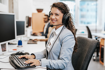Portrait of beautiful smiling female call-center agent with headset working on support in the...